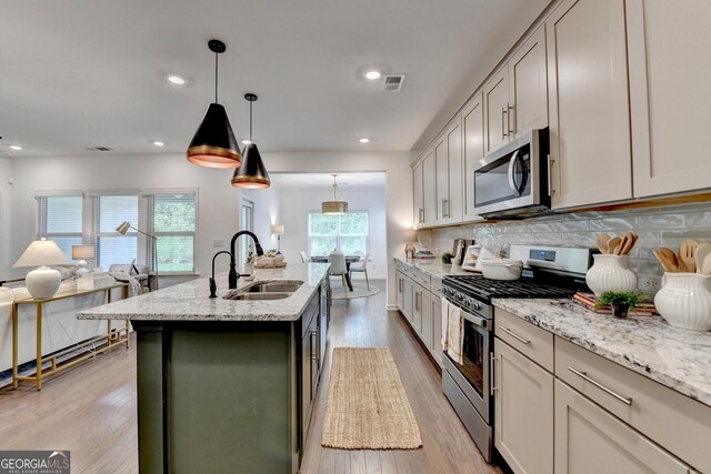 kitchen with appliances with stainless steel finishes, a sink, open floor plan, tasteful backsplash, and light wood-style floors