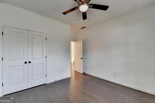 unfurnished bedroom with dark wood-type flooring, baseboards, a closet, and a ceiling fan