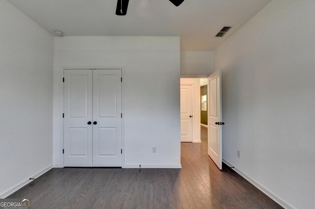 unfurnished bedroom with dark wood-style floors, baseboards, a closet, and a ceiling fan