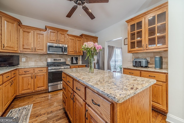 kitchen with a ceiling fan, light wood-type flooring, stainless steel appliances, backsplash, and light stone countertops