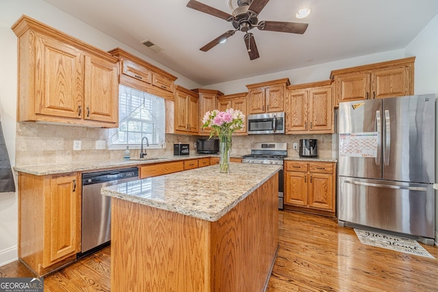 kitchen featuring light stone countertops, stainless steel appliances, a sink, and light wood-style floors
