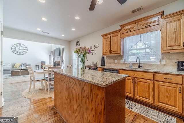 kitchen featuring a center island, backsplash, light stone counters, and a sink