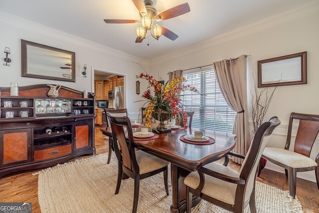 dining space with light wood-style floors, ceiling fan, a wainscoted wall, and ornamental molding