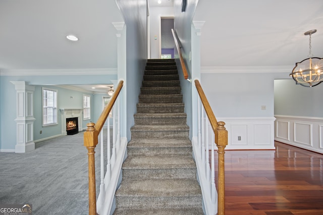 stairway with ornamental molding, a fireplace with flush hearth, a chandelier, and carpet