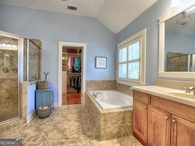 full bathroom with a stall shower, vaulted ceiling, a whirlpool tub, vanity, and a walk in closet