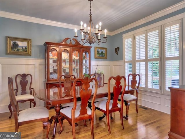 dining area with healthy amount of natural light, a chandelier, a wainscoted wall, a decorative wall, and wood finished floors