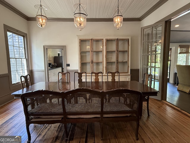 dining space with wood-type flooring, an inviting chandelier, crown molding, and wainscoting