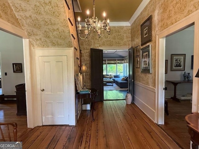 hallway with crown molding, wallpapered walls, an inviting chandelier, and dark wood finished floors