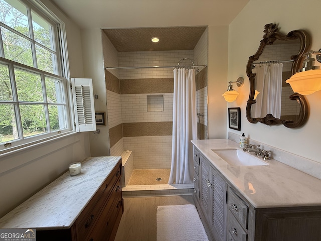 full bathroom with tiled shower, wood finished floors, vanity, and a healthy amount of sunlight