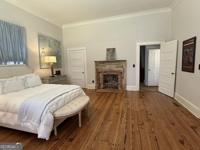 bedroom with hardwood / wood-style flooring, a fireplace with flush hearth, baseboards, and ornamental molding