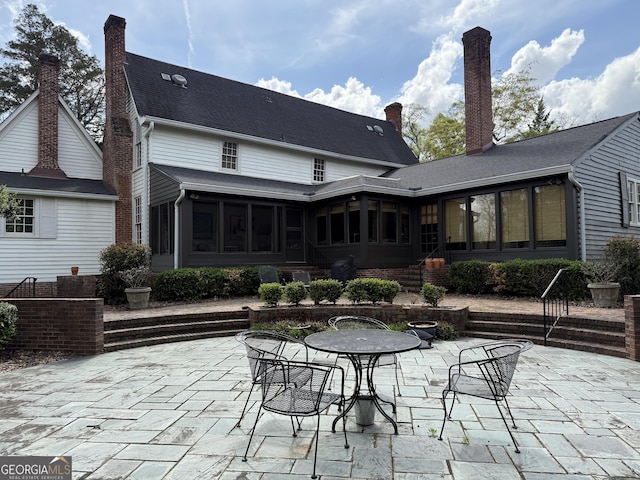 back of property with a sunroom, a chimney, a patio, and outdoor dining area