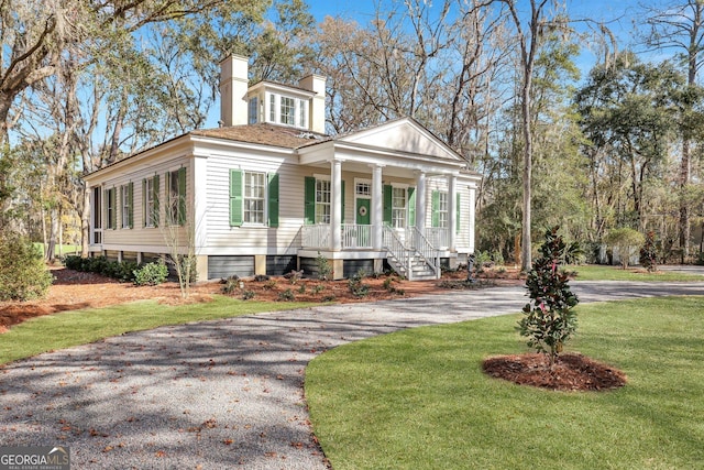 192 Myrtle Grove Ln, Richmond Hill, GA 31324 - neoclassical / greek revival house featuring driveway, covered porch, a front yard, and a chimney