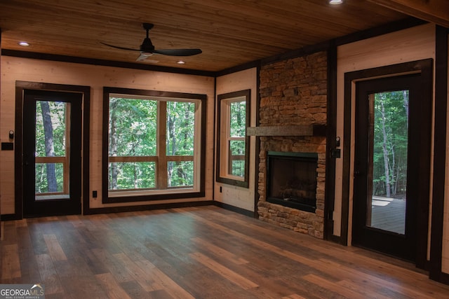 unfurnished living room with plenty of natural light, ceiling fan, a stone fireplace, wood finished floors, and wooden ceiling
