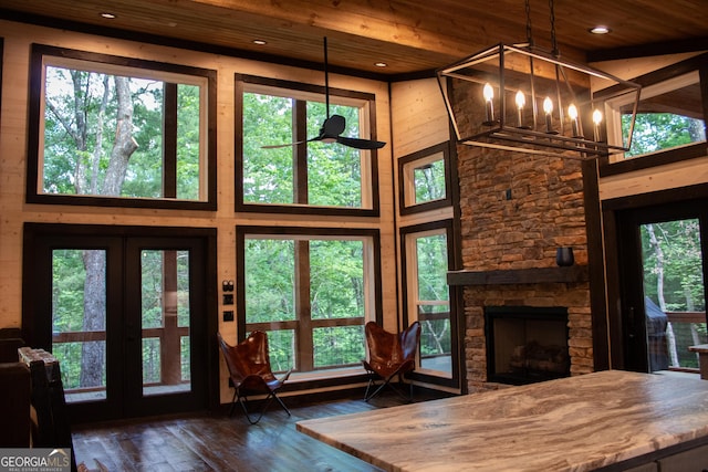 unfurnished living room featuring a stone fireplace, hardwood / wood-style flooring, wooden ceiling, an inviting chandelier, and a high ceiling