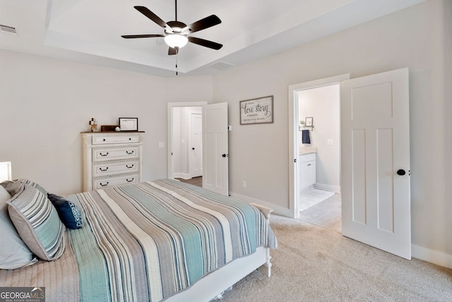 bedroom with a tray ceiling, visible vents, light carpet, ensuite bath, and baseboards