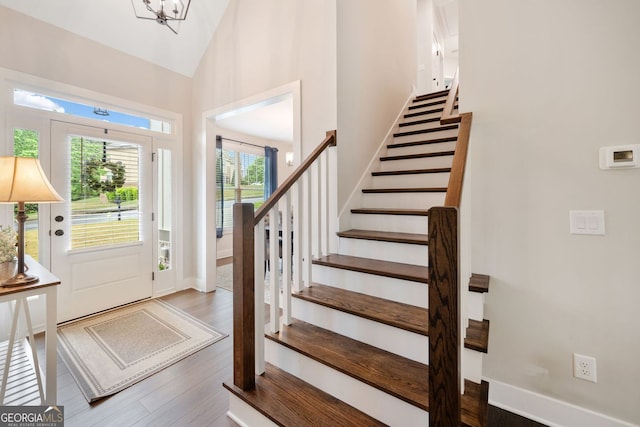 foyer with high vaulted ceiling, wood finished floors, baseboards, and stairs