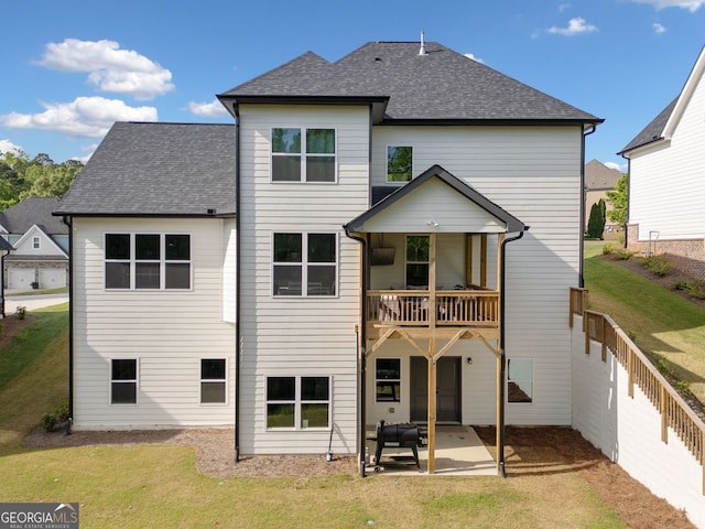 rear view of house with a balcony, a lawn, a shingled roof, fence, and a patio