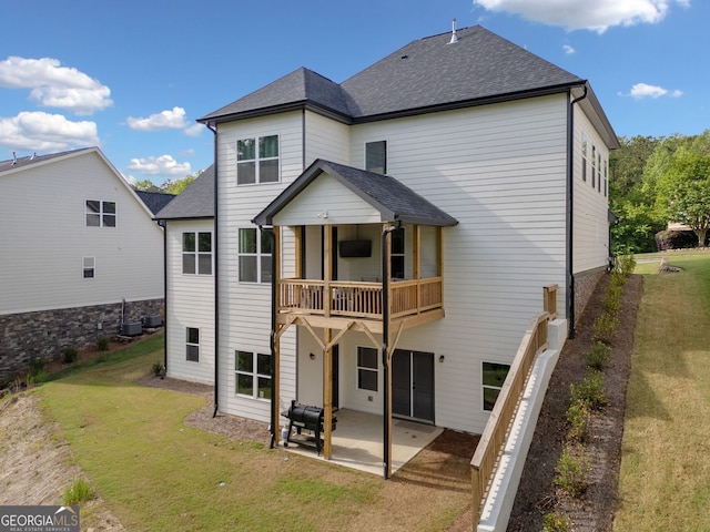 rear view of house featuring a yard, a patio area, a shingled roof, and a balcony