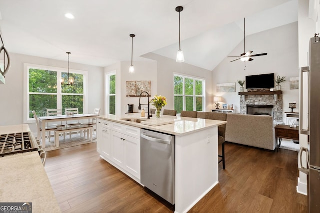 kitchen with white cabinets, a stone fireplace, a sink, appliances with stainless steel finishes, and ceiling fan with notable chandelier