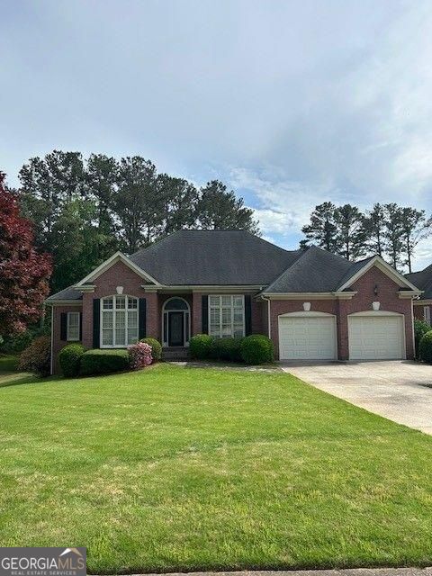 ranch-style house with an attached garage, a front lawn, brick siding, and concrete driveway