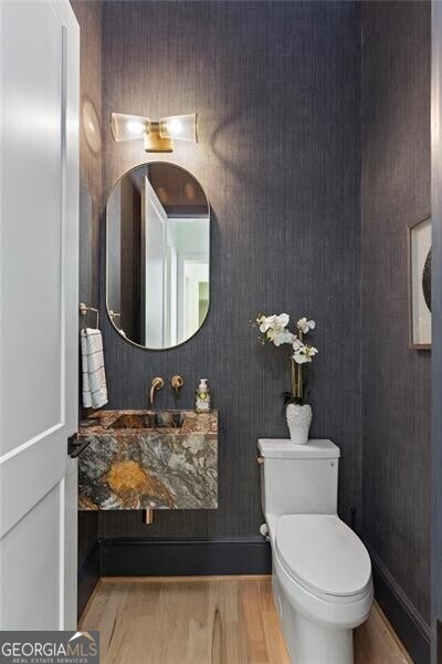 half bath with toilet, wood finished floors, and baseboards