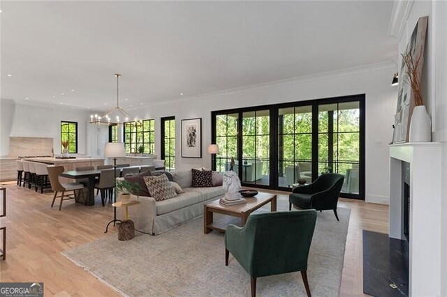living area with light wood-type flooring, a high end fireplace, a chandelier, and ornamental molding