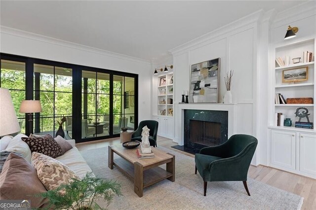 living room with built in shelves, ornamental molding, light wood-style floors, and a fireplace