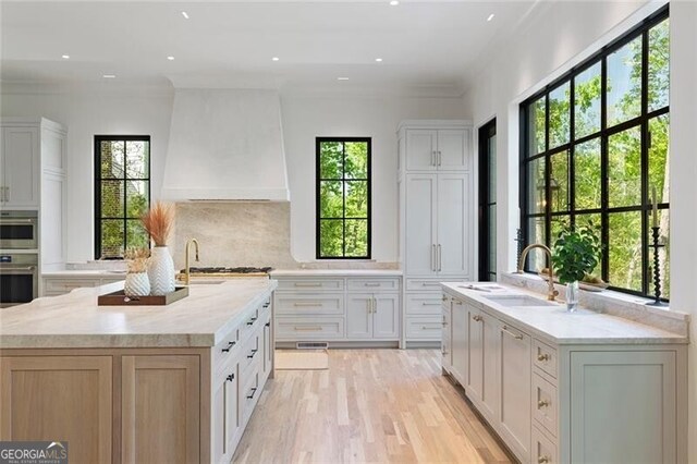 kitchen featuring recessed lighting, an island with sink, backsplash, a sink, and light wood-style floors
