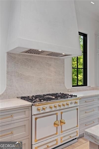 kitchen featuring decorative backsplash, light wood-type flooring, premium range hood, white cabinets, and range with two ovens
