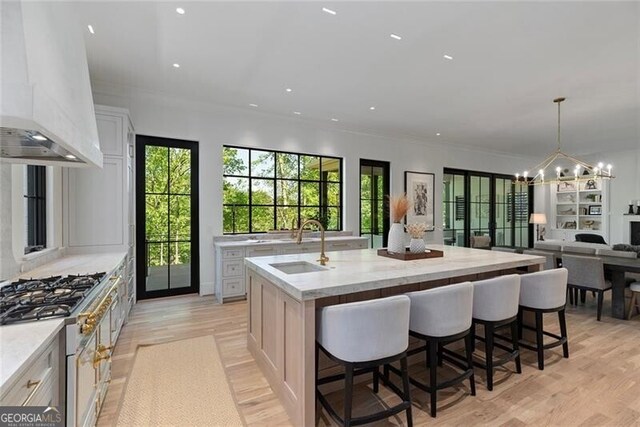 kitchen with range with gas stovetop, a sink, open floor plan, a large island with sink, and custom range hood
