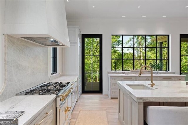 kitchen featuring light wood finished floors, light stone counters, a sink, range with gas stovetop, and custom range hood