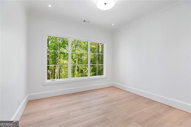 spare room featuring baseboards, ornamental molding, light wood finished floors, and visible vents