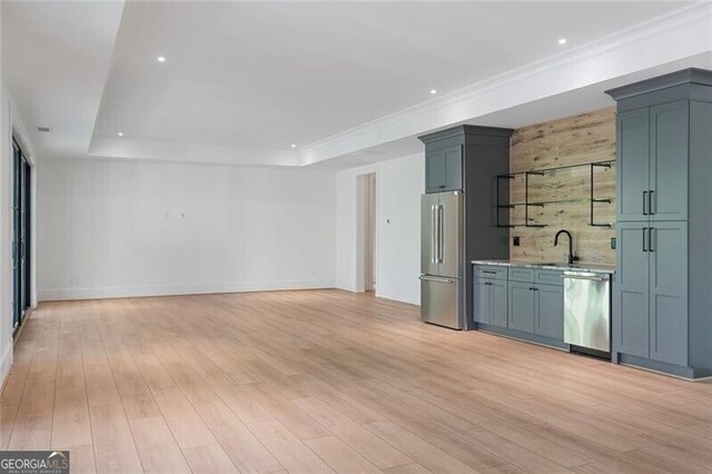 interior space with a tray ceiling, a sink, baseboards, light wood-style flooring, and appliances with stainless steel finishes