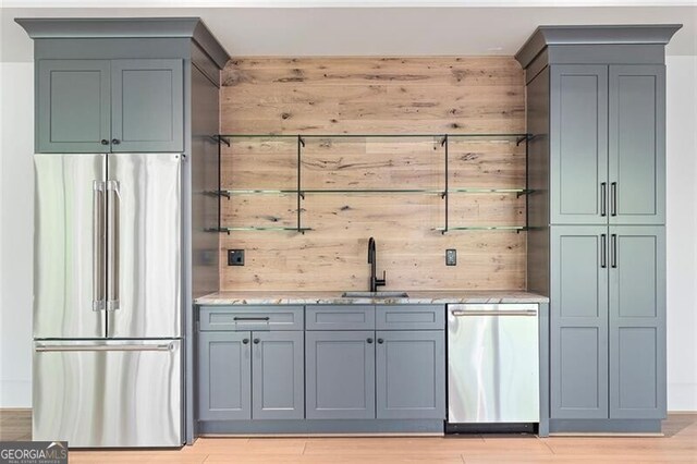 bar with a sink, light wood-style floors, wooden walls, indoor wet bar, and appliances with stainless steel finishes