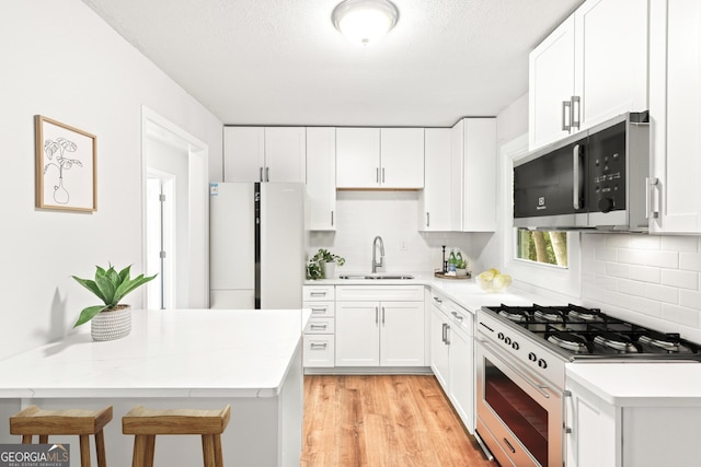 kitchen featuring light wood-style floors, tasteful backsplash, a sink, and white appliances