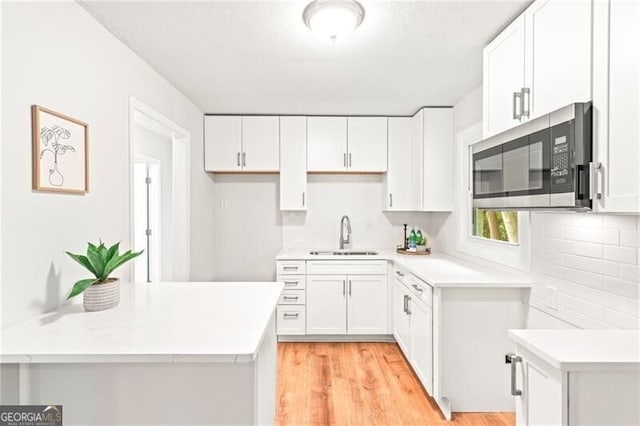 kitchen featuring light wood-style flooring, a sink, stainless steel microwave, backsplash, and white cabinetry