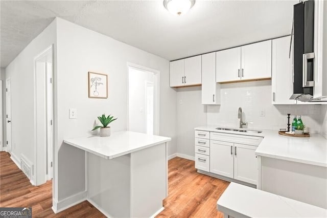 kitchen with white cabinets, a sink, light countertops, and light wood-type flooring