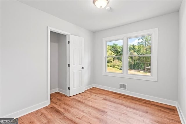spare room with light wood-type flooring, visible vents, and baseboards