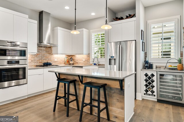 986 Mauldin St SE, Atlanta, GA 30316 - kitchen with wall chimney range hood, appliances with stainless steel finishes, a breakfast bar, a sink, and beverage cooler