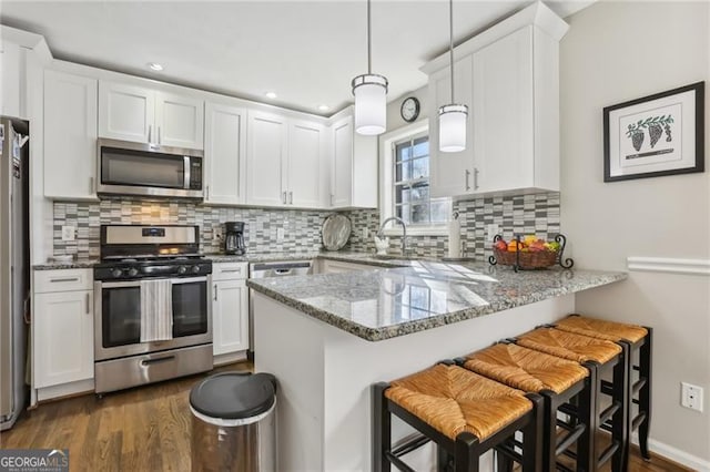 kitchen featuring white cabinets, a peninsula, appliances with stainless steel finishes, and dark wood finished floors