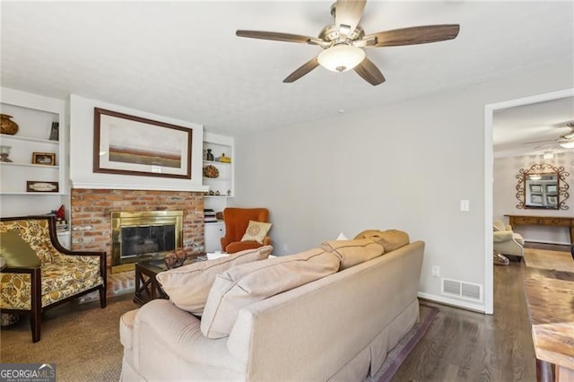 living area with wood finished floors, ceiling fan, built in features, a brick fireplace, and visible vents