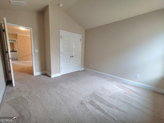 unfurnished bedroom featuring vaulted ceiling, a closet, light carpet, baseboards, and visible vents