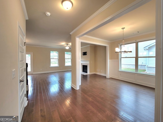 unfurnished living room featuring dark wood-style floors, baseboards, ceiling fan with notable chandelier, crown molding, and a fireplace