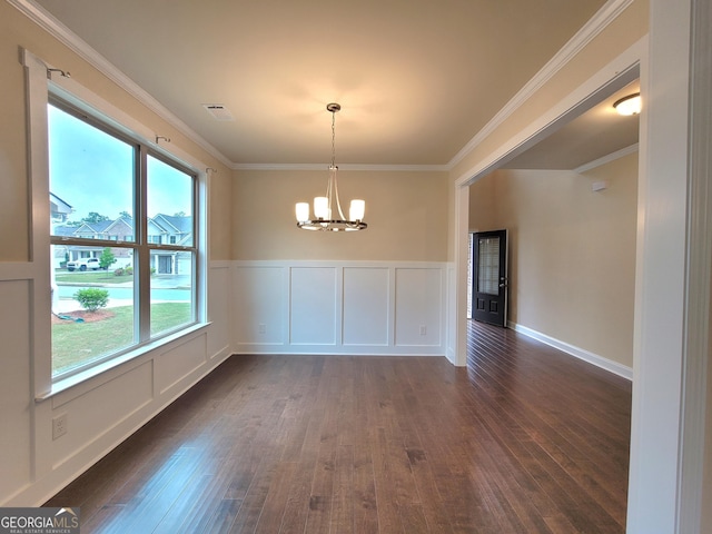 unfurnished dining area featuring dark wood finished floors, ornamental molding, a decorative wall, wainscoting, and a chandelier