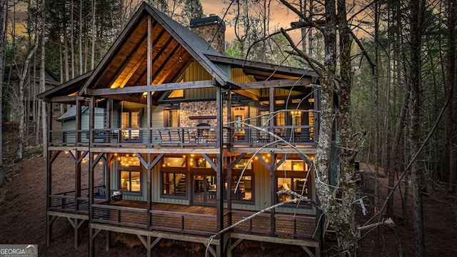 back of property at dusk featuring board and batten siding, a chimney, a balcony, and a deck