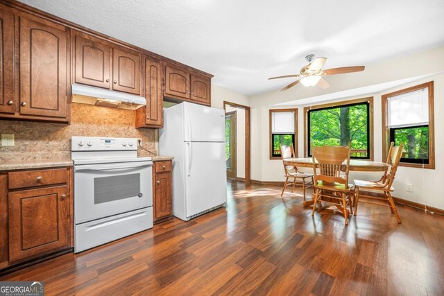 kitchen with dark wood-style floors, under cabinet range hood, a ceiling fan, white appliances, and decorative backsplash
