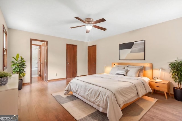 bedroom with light wood-style flooring, baseboards, ensuite bathroom, and a ceiling fan
