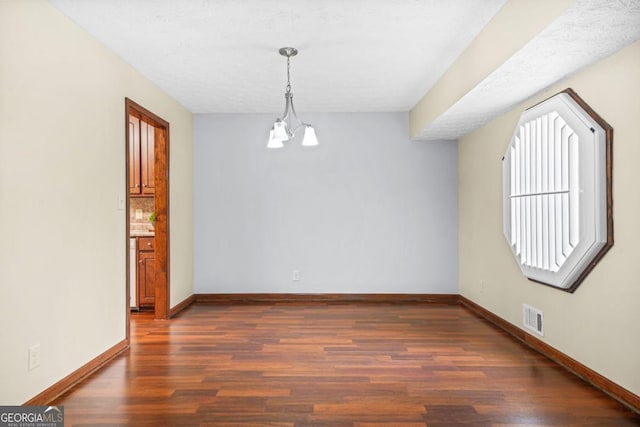 empty room featuring baseboards, a notable chandelier, wood finished floors, and visible vents