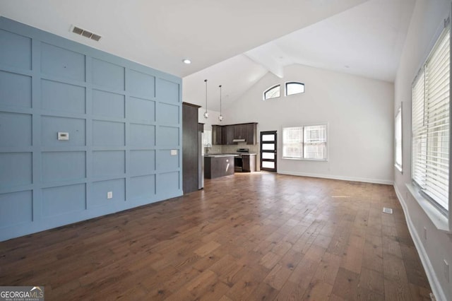 unfurnished living room featuring high vaulted ceiling, a decorative wall, dark wood-style flooring, and visible vents