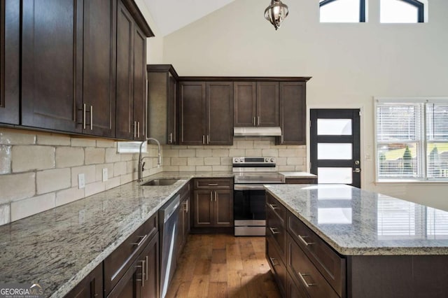 kitchen featuring stainless steel appliances, a sink, dark wood finished floors, light stone counters, and under cabinet range hood